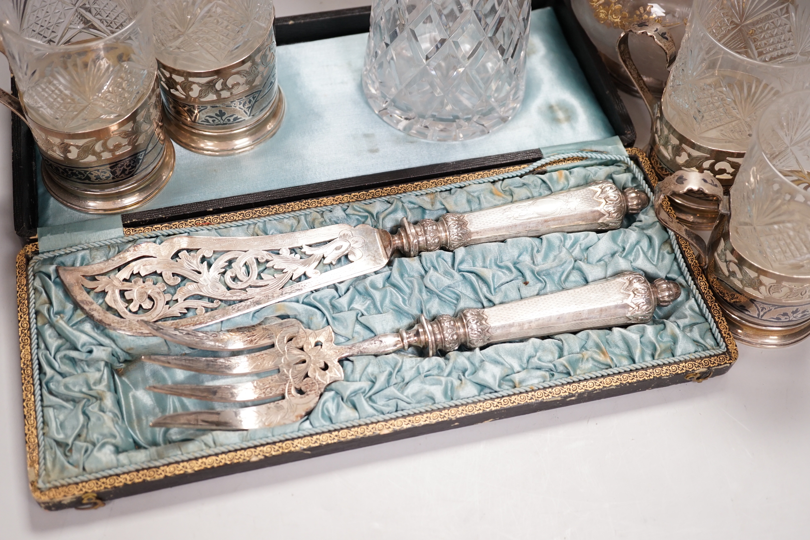 Two claret jugs, one with gilt decoration, four silver plated cup holders with glass liners and silver plated fish servers, the largest 32cm high